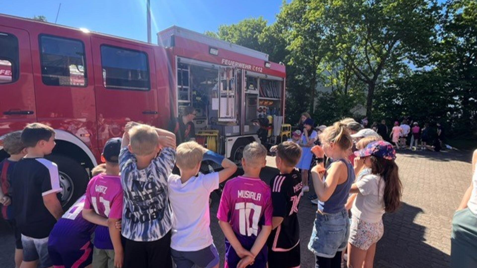 Eine Gruppe Kinder steht im Halbkreis um ein geöffnetes Einsatzfahrzeug der Feuerwehr