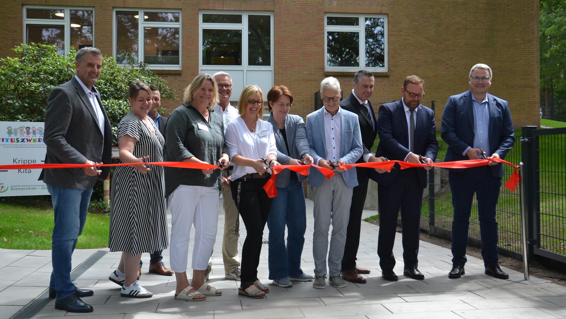 Vertreter der Stadt Zeven, der Kita Vituszwerge, der Ostemed und der Elbe-Kliniken zerschneiden mit Landrat Marco Prietz vor der neuen Einrichtung im ehemaligen Zevener Krankenhaus ein rotes Band.  