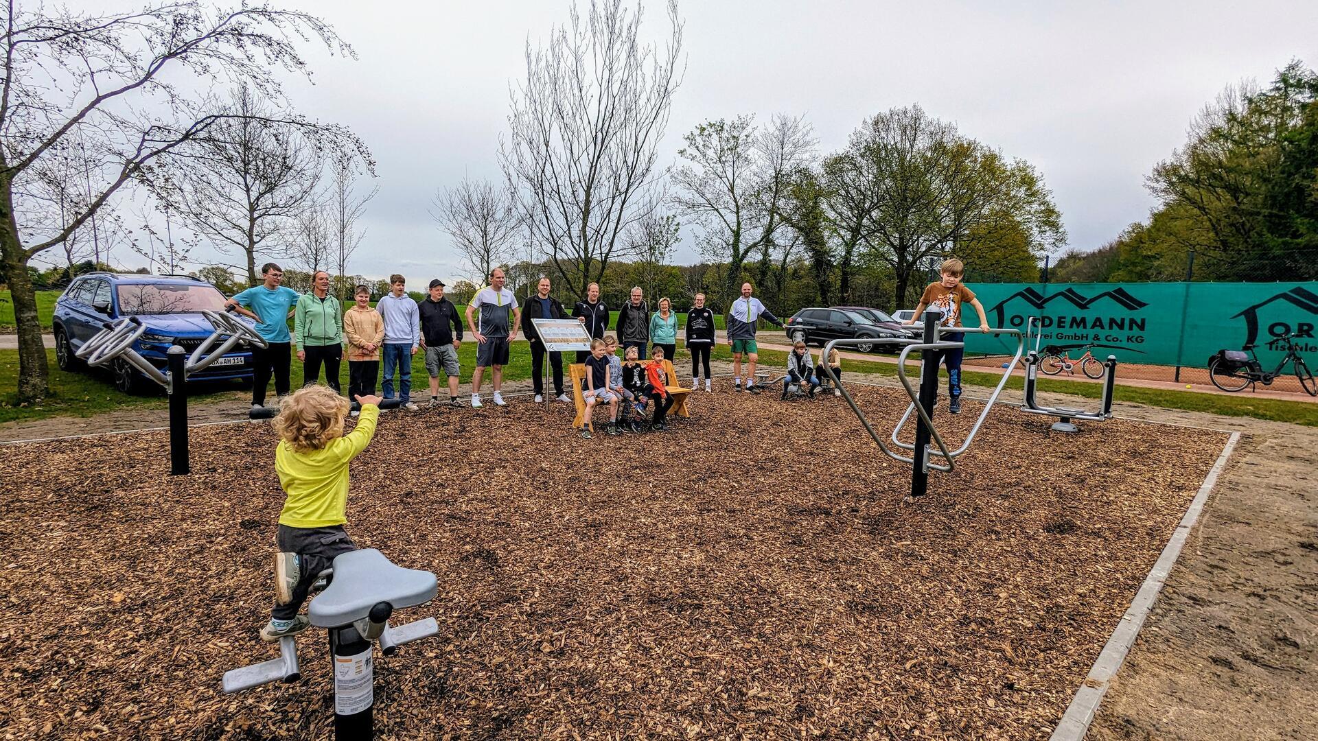 Kinder testen die Geräte auf dem Outdoor-Fitnesspark neben dem Appelner Sportplatz. Im Hintergrund stehen einige Erwachsene. 