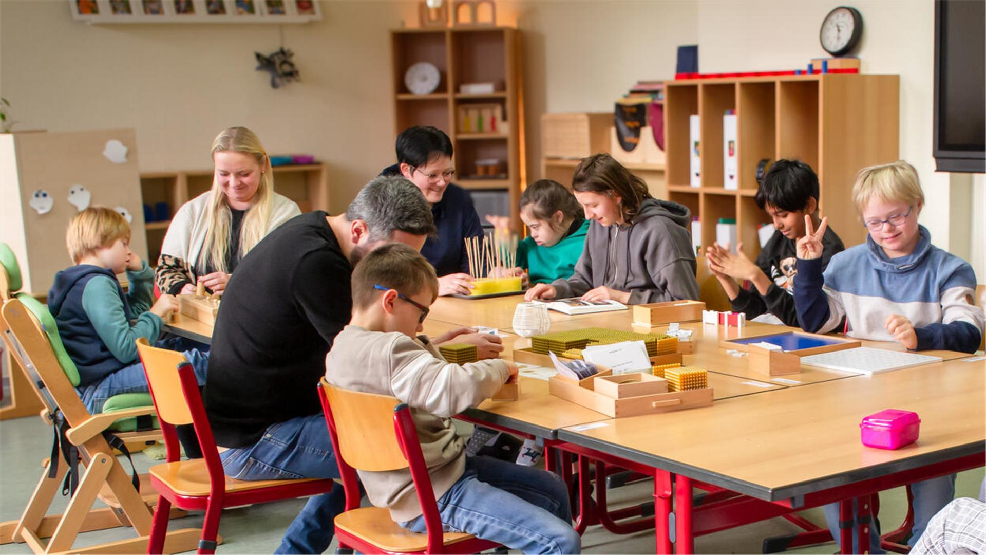 Schülerinnen und Schüler sitzen mit ihren Betreuern in einem Raum an einem Tisch