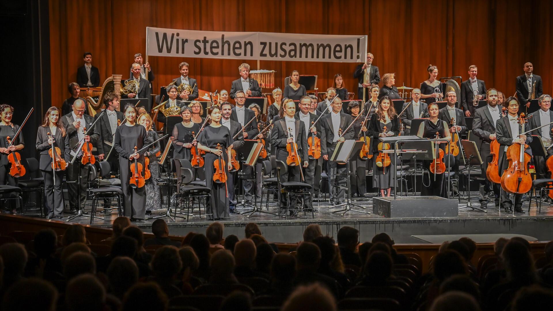 Vor dem 3. Sinfoniekonzert am Montag und Dienstag demonstrierten die Orchestermitglieder mit einem Banner ihre Geschlossenheit im Konflikt. Dafür gab es viel Beifall vom Publikum.