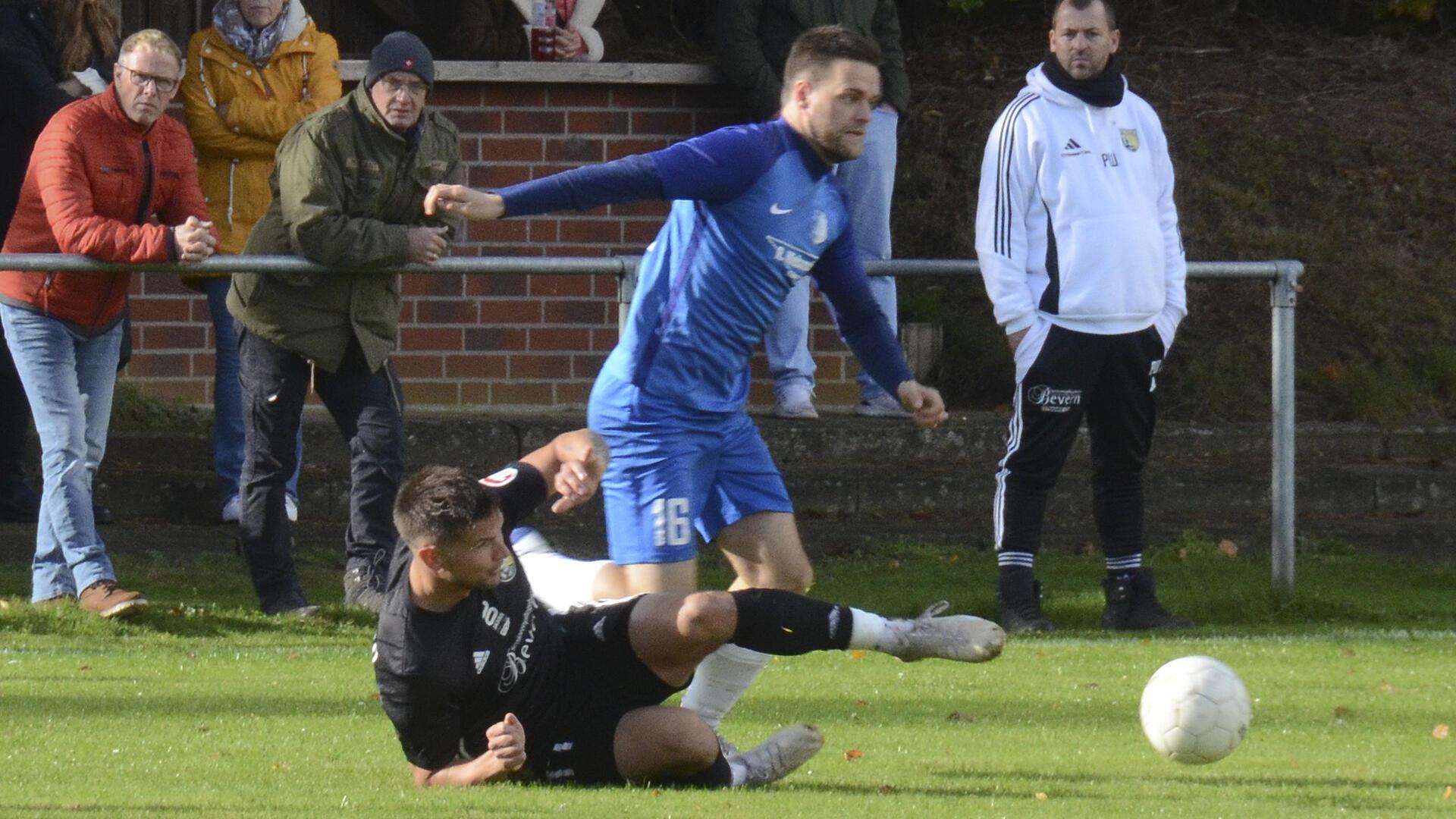 Während TSV-Angreifer Justin Brünjes FC A/E-Gegenspieler Marten Brandt den Ball wegspitzelt, schaut Beverns Trainer Patrick Wellbrock im Hintergrund zu.