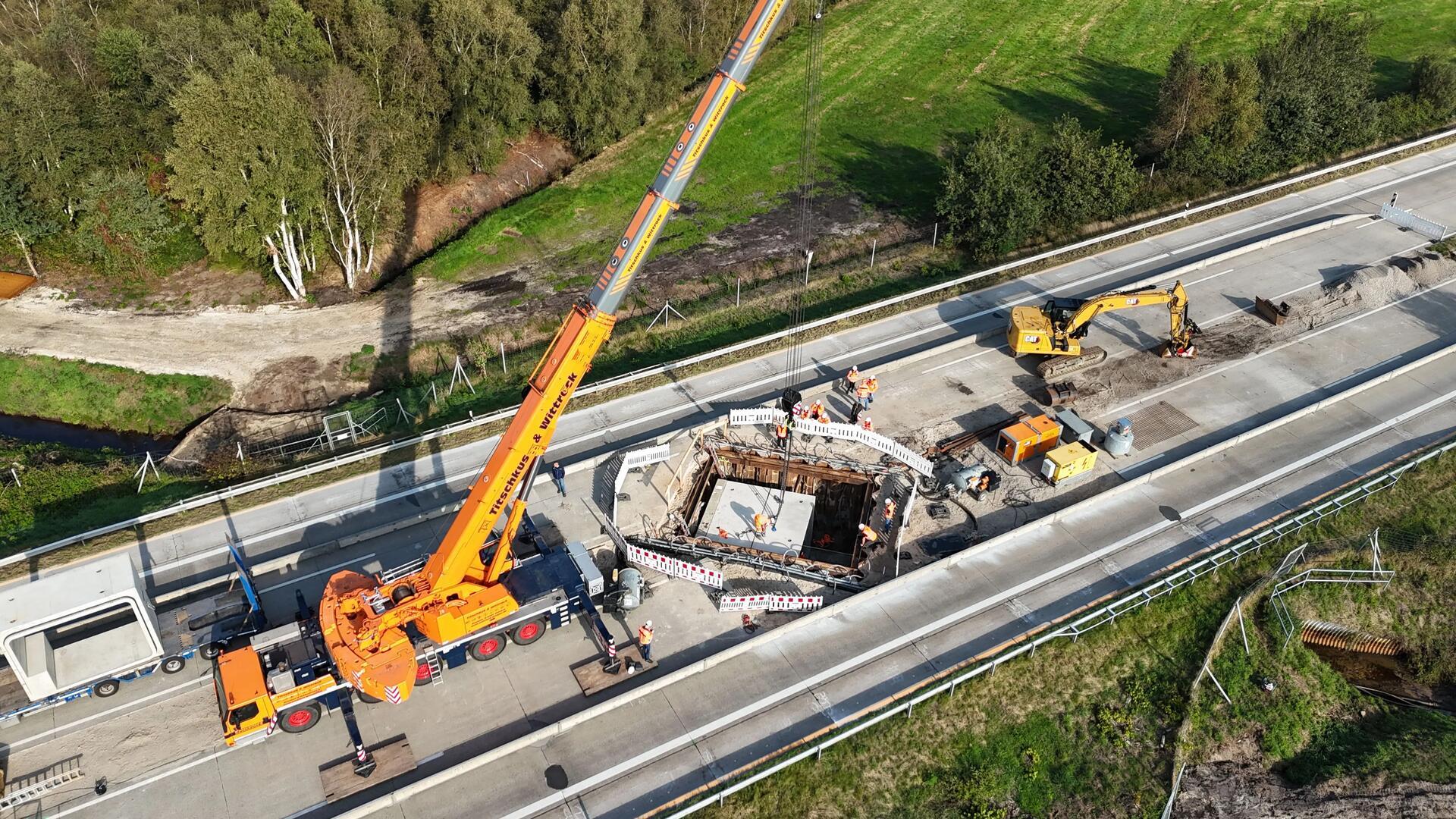 Ein großes Betonteil wird über einer Autobahn von einem Kran angehoben.