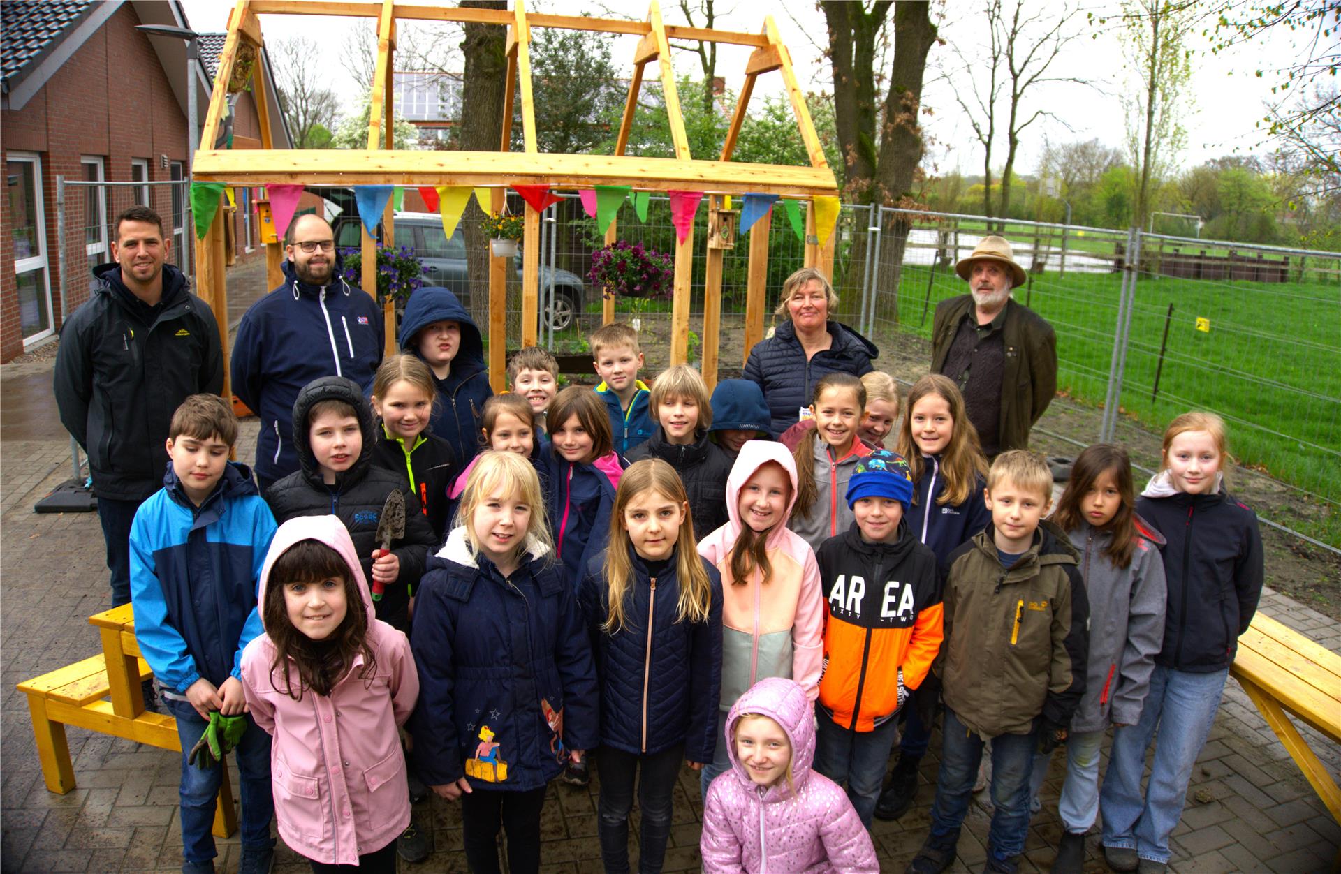 Eine dritte Klasse und vier Erwachsene stehen vor einem hölzernen Gerüst eines Green-House.