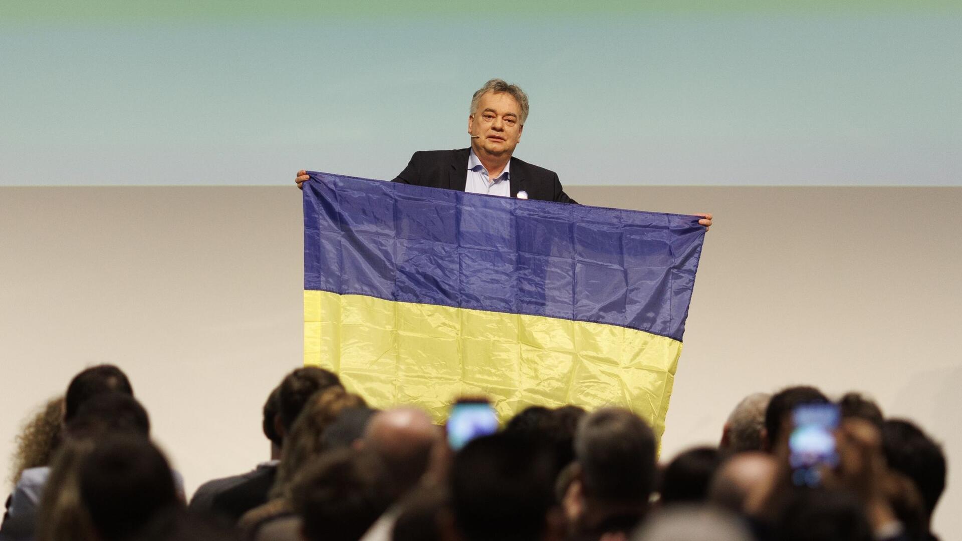 Werner Kogler (Grüne), Vizekanzler von Österreich, steht mit einer Fahne der Ukraine auf der Bühne beim Bundeskongress seiner Partei, am zweiten Jahrestag der russischen Invasion.