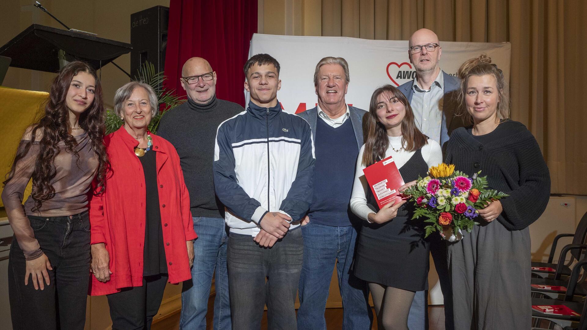 Acht junge und ältere Menschen stehen nebeneinander vor einem Transparent mit der Aufschrift "AWO Bremerhaven"