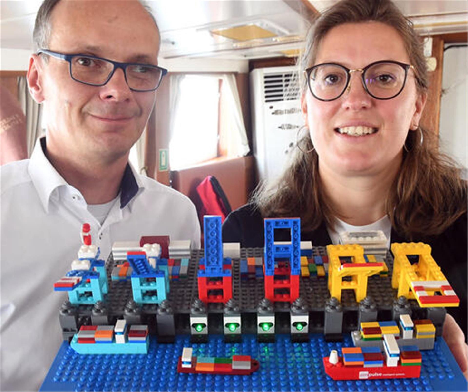 Ein Mann und eine Frau zeigen ein Lego-Bauwerk in die Kamera.