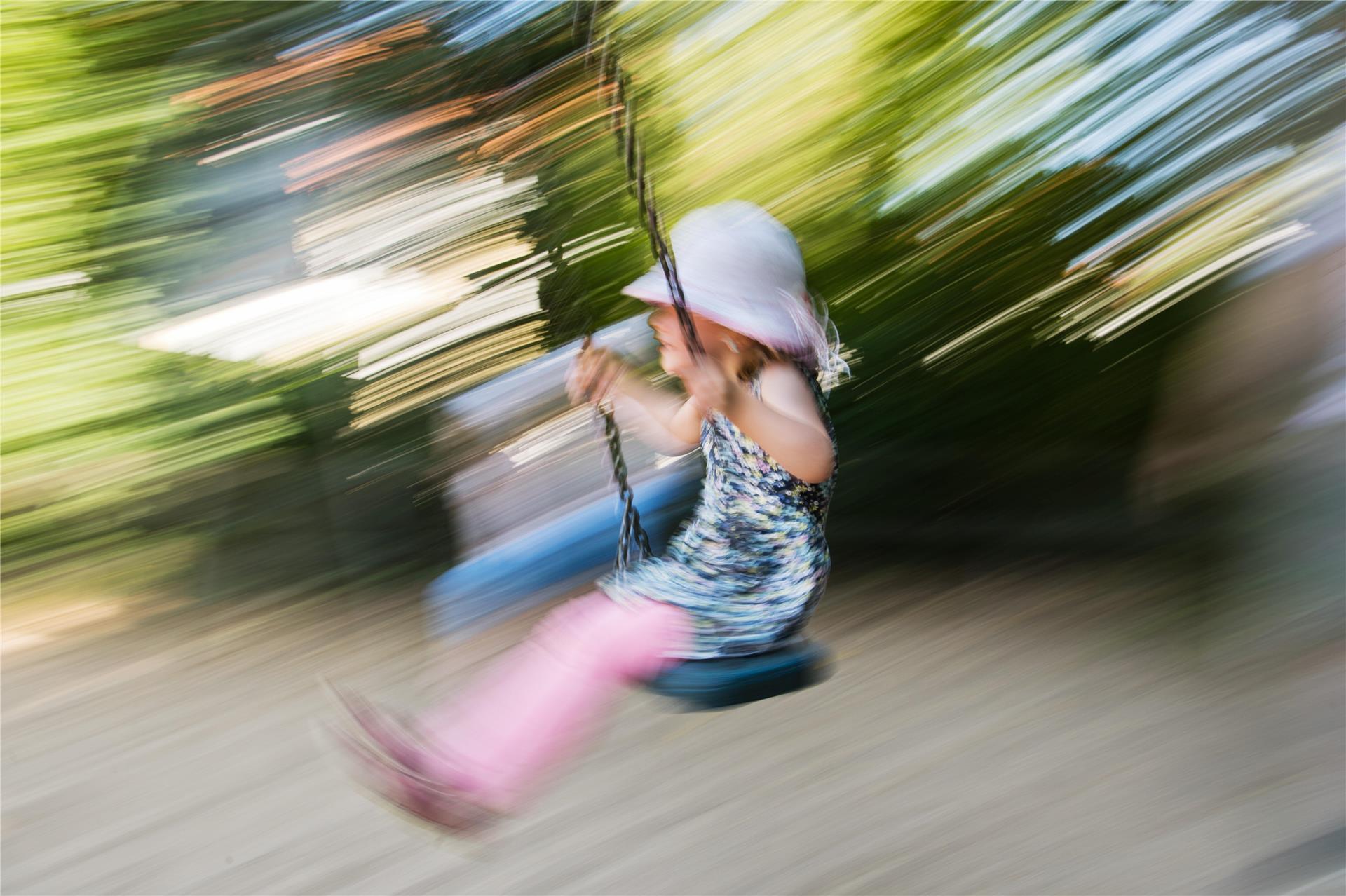  Ein kleines Mädchen schaukelt auf einem Spielplatz (Aufnahme mit langer Verschlusszeit). 