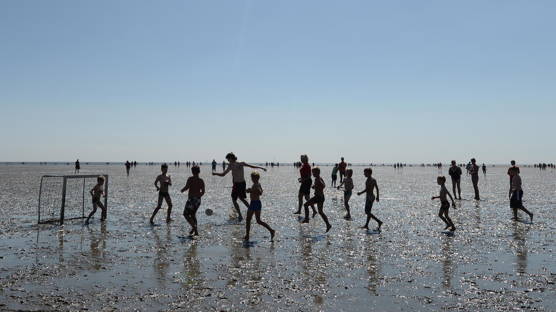 Kinder spielen im Watt Fußball. Im Ferienpass der Gemeinde Wurster Nordseeküste wird Wattfußball angeboten.