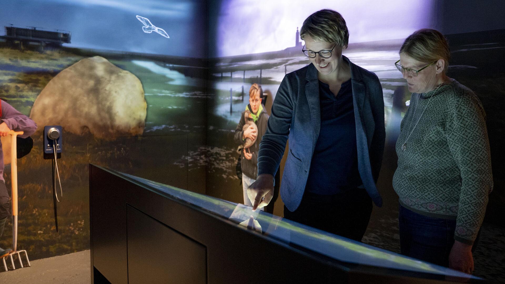 Zwei Frauen stehen in einem Ausstellungsraum und schauen auf eine interaktive Ausstellungstafel