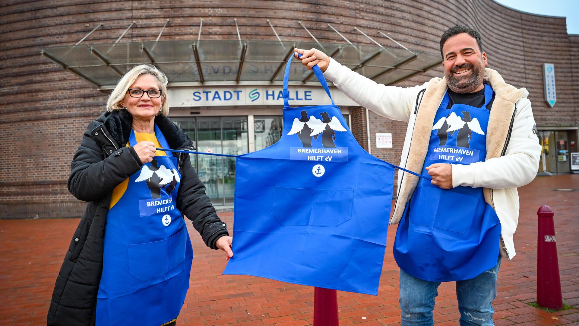 Gaby Treschok und Alexis Vaiou vom Verein "Bremerhaven hilft" halten die Stellung im Namen der beiden anonymen "Engel" - den Spendern des großen Weihnachtsessens für rund 1200 Bedürftige in der Bremerhavener Stadthalle. Die dritte Schürze bleibt an diesem Termin nur deshalb "bauchlos", weil der Dritte im Helfer-Trio, Manfred Jabs, erkrankt ist.